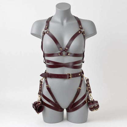 Ensemble de soumission fétiche pour chiot Alpha Restraint composé d'un baudrier cage de poitrine croisé, d'une large ceinture abdominale avec sangles de cuisses et d'entraves poignets en simili cuir bordeaux de face sur mannequin.